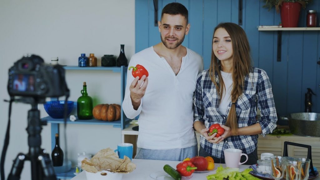 Young attractive couple recording video blog about vegetarian healthy food on dslr camera in the kitchen at home